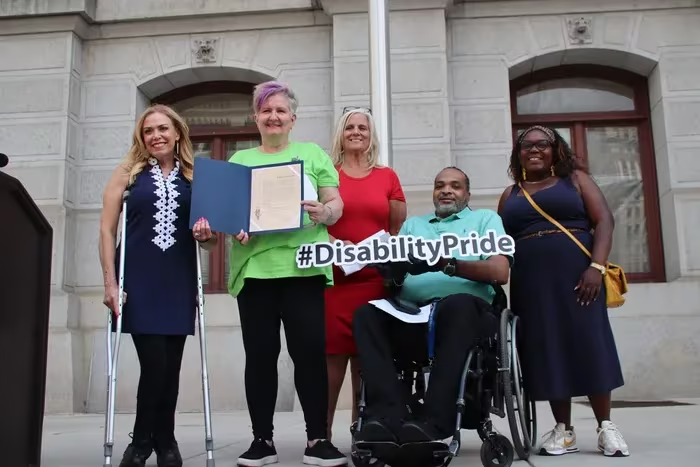 City Representative Sheila Hess, Vicki Landers, founder and executive director of Disability Pride PA, City Commissioners Chair Lisa Deeley, Chuck Horton, Disability Pride board president, and Councilmember Kendra Brooks pose at the Disability Pride flag raising outside City Hall 
Kathleen Melville