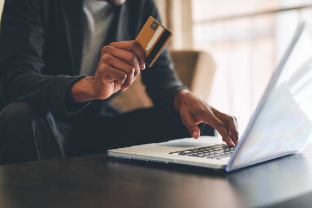 A person holding a laptop on their lap while using a blue ATM card to purchase something on their smartphone