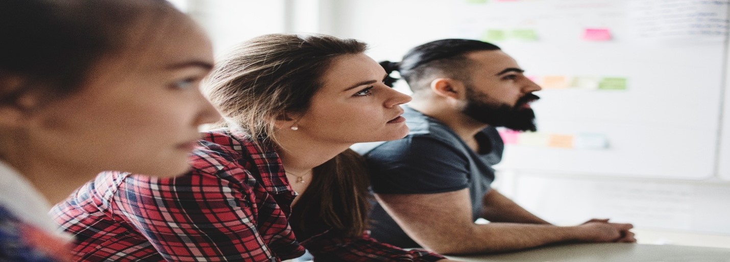 Close-up of three casual professionals watching presentation in creative office