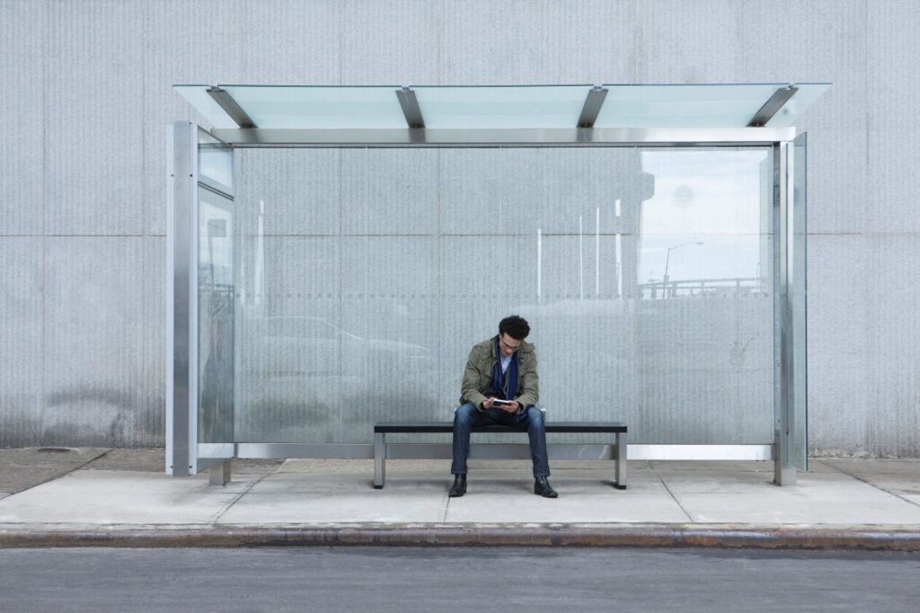 Person sitting alone at bus stop using cellphone
