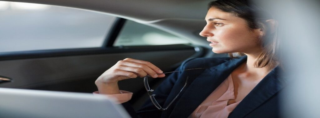 A person sitting in a car as a passenger, holding a pair of eyeglasses and looking out the window