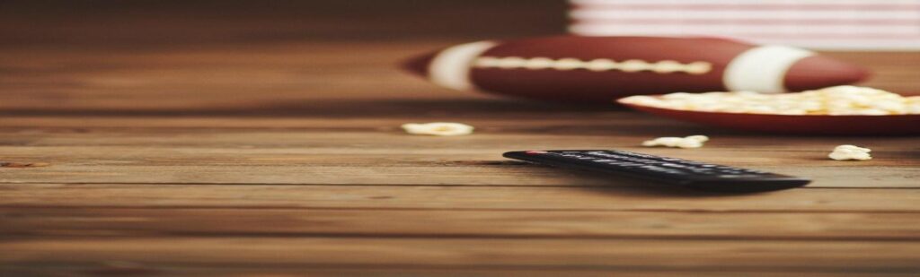 Remote control, popcorn and American football on wood surface