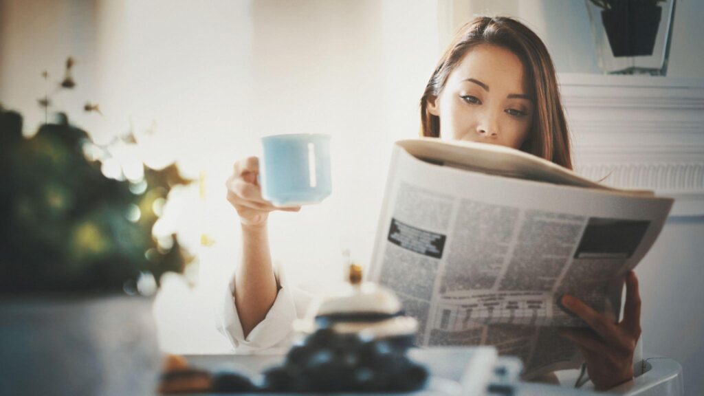 Person reading the newspaper and drinking from a mug