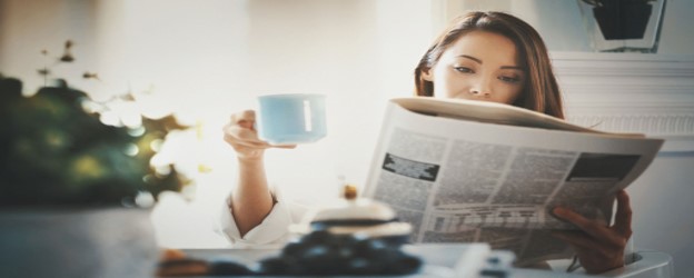 Person reading the newspaper and drinking from a mug