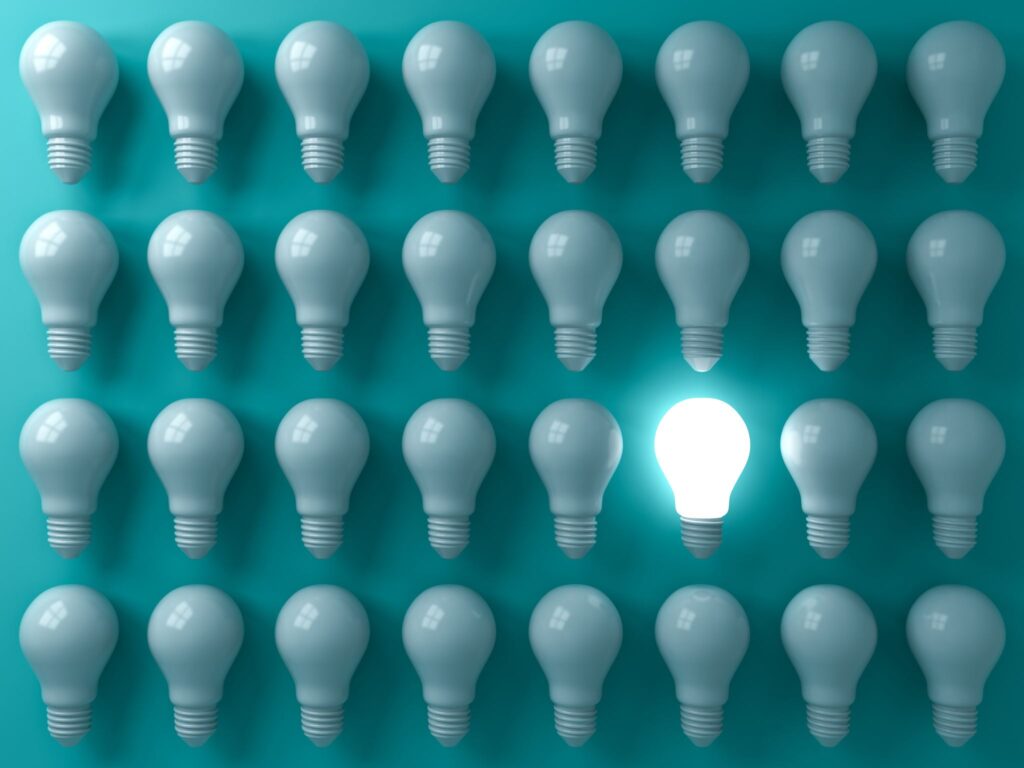 One glowing light bulb among rows of unlit bulbs